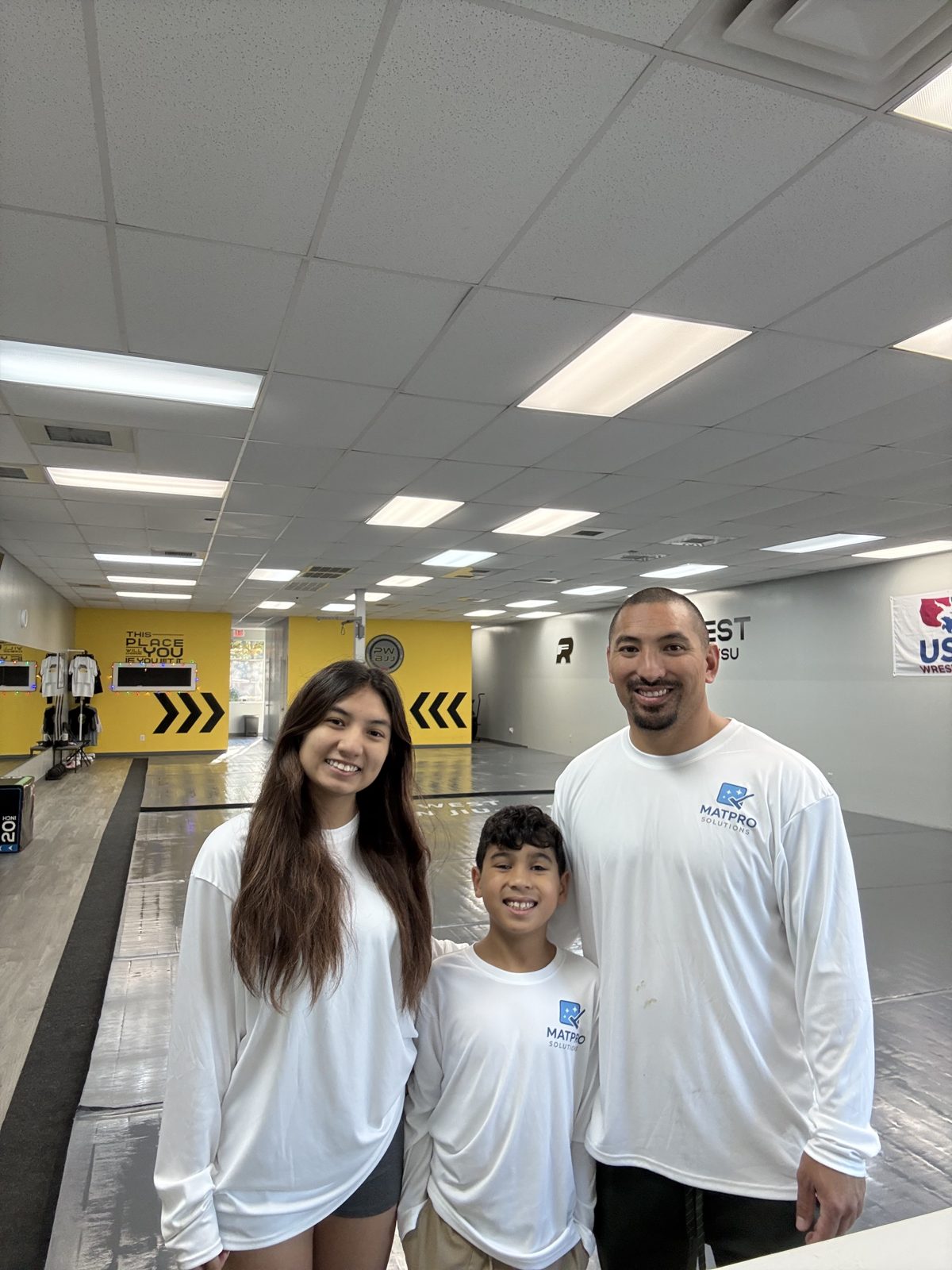 The Mat Pro Solutions family in Mat Pro shirts standing on a clean jiu jitsu mat